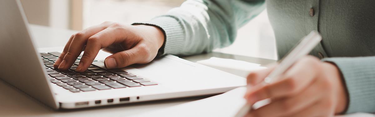 Woman working on computers and writing on notepad with pen in an office.